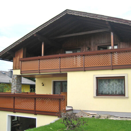 Zweistöckiges Haus mit Balkon und großem Holzgeländer im Grünen, typisch alpenländisch. HANSEL.kraus metalltechnik gmbh