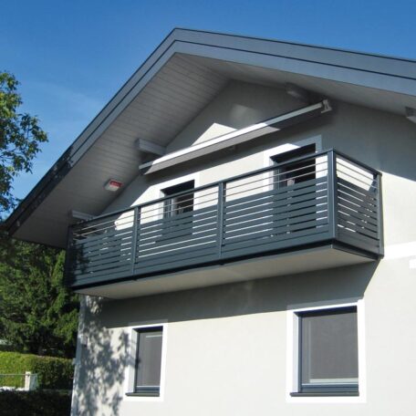 Moderner Balkon mit Metallgeländer an weißem Einfamilienhaus unter blauem Himmel. de HANSEL.kraus metalltechnik gmbh