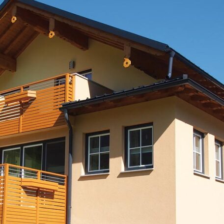 Modernes Einfamilienhaus mit Holzbalkon und Satteldach, klare Linien bei Sonnenschein. Sprache: de HANSEL.kraus metalltechnik gmbh