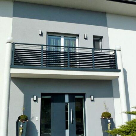 Modernes Haus mit grauem Balkon und großen Fenstern, Eingangstüren und Pflanzen davor. de HANSEL.kraus metalltechnik gmbh