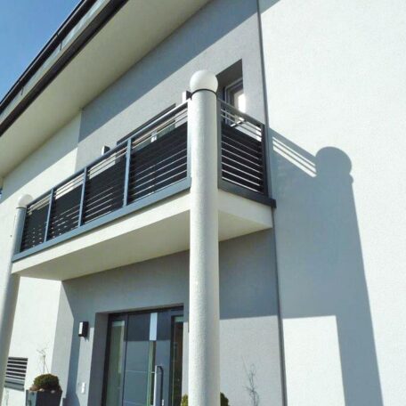 Moderner Balkon mit Glasgeländer an weißer Hausfassade, im Sonnenlicht, Eingangsbereich darunter sichtbar. de HANSEL.kraus metalltechnik gmbh