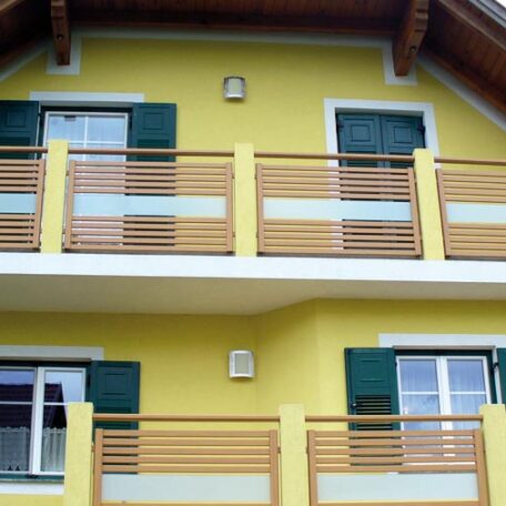 Zweistöckiges gelbes Haus mit grünem Fensterladen und Holzbalkonen, modernes Wohngebäude. HANSEL.kraus metalltechnik gmbh