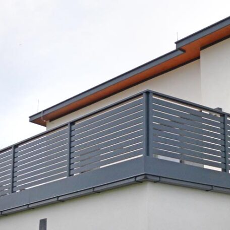 Moderner Balkon mit grauem Metallgeländer an weißer Hausfassade unter bewölktem Himmel. HANSEL.kraus metalltechnik gmbh
