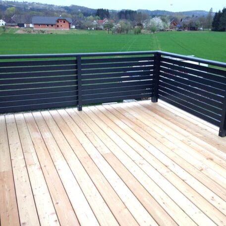 Holzterrasse mit modernem, schwarzem Geländer, ländliche Aussicht auf grüne Wiese und Gebäude. HANSEL.kraus metalltechnik gmbh