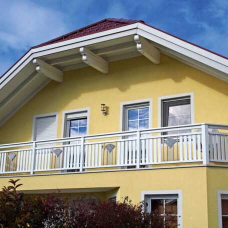 Gelbes Einfamilienhaus mit Balkon und weißen Fenstern, blauer Himmel im Hintergrund. HANSEL.kraus metalltechnik gmbh