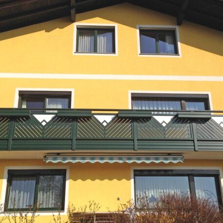 Gelbes Haus mit grünem Balkon, weißen Fenstern und Markise an der Fassade. HANSEL.kraus metalltechnik gmbh