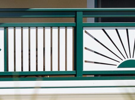 Grünes Metallgeländer mit weißen Elementen und dekorativem Sonnenstrahl-Muster auf einer Terrasse. HANSEL.kraus metalltechnik gmbh