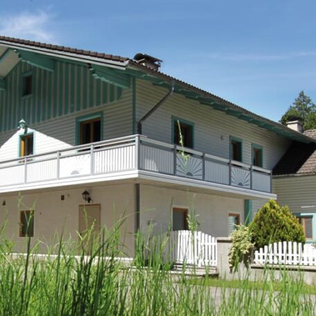 Modernes Einfamilienhaus mit Balkon, Garten und weißem Zaun bei sonnigem Wetter. de HANSEL.kraus metalltechnik gmbh
