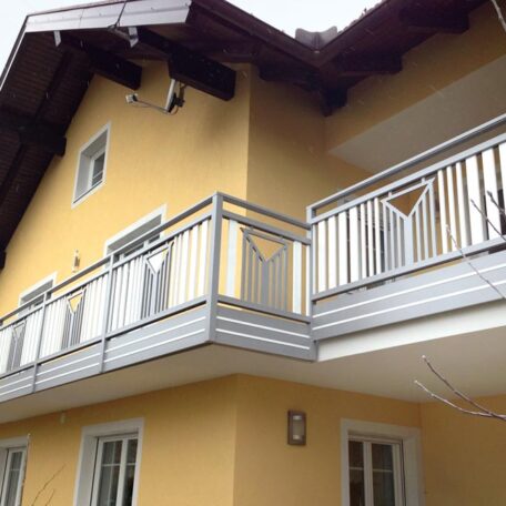 Zweistöckiges gelbes Haus mit weißem Balkon und dunklem Holzdach, große Fenster. de HANSEL.kraus metalltechnik gmbh