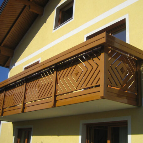 Holzbalkon mit dekorativem Muster an gelber Hausfassade, sonniger Tag, modernes Design. HANSEL.kraus metalltechnik gmbh