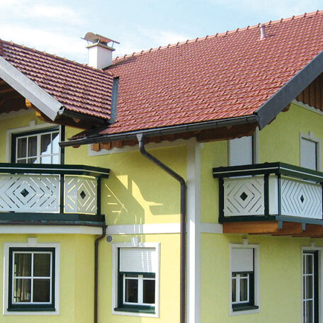 Gelbes Haus mit rotem Satteldach, weißen Fenstern und zwei Holz-Balkonen. HANSEL.kraus metalltechnik gmbh
