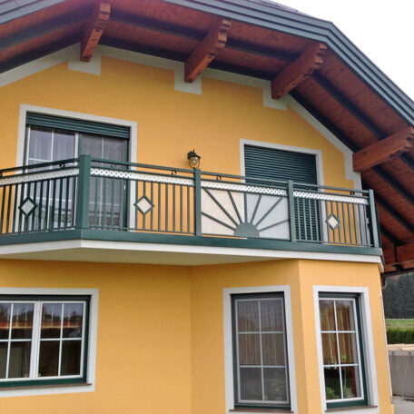 Gelbes Einfamilienhaus mit grünem Balkon und großen Fenstern unter einem Satteldach. HANSEL.kraus metalltechnik gmbh
