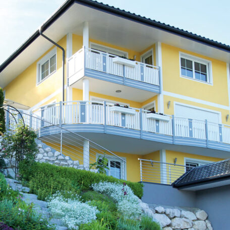 Zweistöckiges gelbes Haus mit weißen Balkonen und großem Garten an Hanglage. HANSEL.kraus metalltechnik gmbh