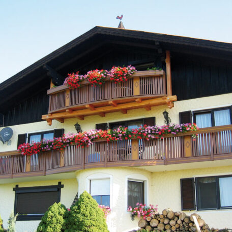 Zweistöckiges Haus mit Holzbalkonen und bunten Blumenkästen an der Fassade. HANSEL.kraus metalltechnik gmbh
