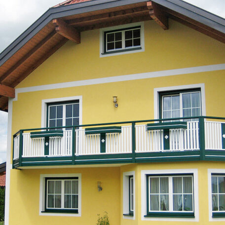 Gelbes Haus mit Balkon, weißen Fenstern und grünem Geländer, modernes Einfamilienhaus. HANSEL.kraus metalltechnik gmbh