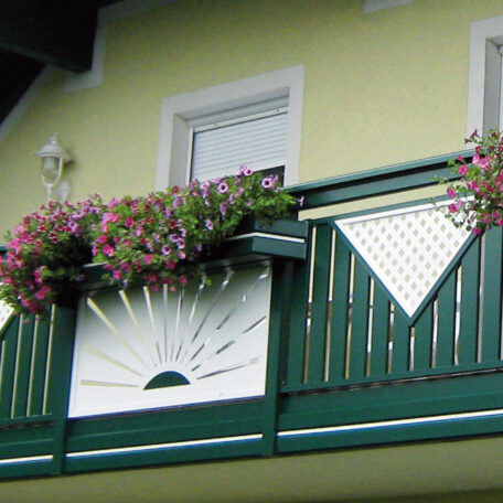 Balkon mit grünem Geländer, Blumenkästen und dekorativem Sonnensymbol vor gelber Hauswand. HANSEL.kraus metalltechnik gmbh