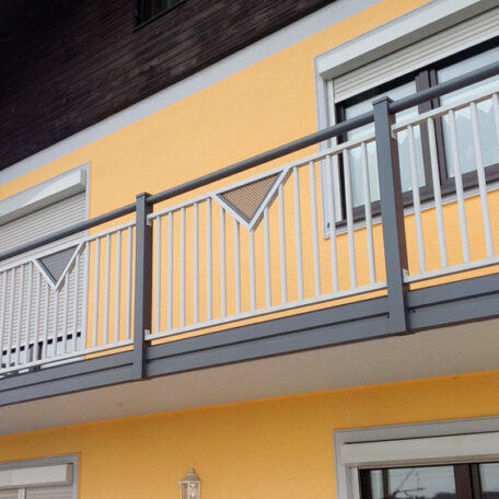 Moderner Balkon mit grauem Metallgeländer und geometrischem Muster an gelber Hausfassade. de HANSEL.kraus metalltechnik gmbh