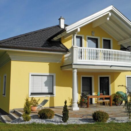 Modernes gelbes Einfamilienhaus mit Balkon, Garten und Terrasse unter blauem Himmel. HANSEL.kraus metalltechnik gmbh