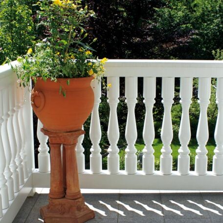 Blumentopf mit gelben Blumen steht auf Terrasse vor weißem Geländer im Sonnenschein. HANSEL.kraus metalltechnik gmbh