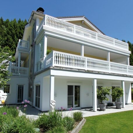 Modernes weißes Mehrfamilienhaus mit großzügigen Balkonen und Garten vor bewaldeter Kulisse. HANSEL.kraus metalltechnik gmbh