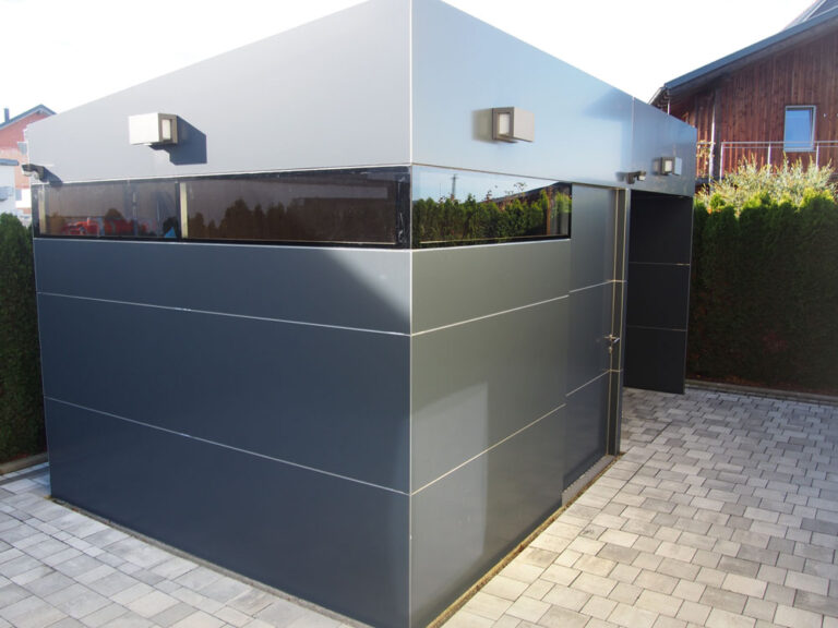 Moderne Fertiggarage aus Metall mit großem Fenster auf gepflastertem Grundstück bei Tageslicht. HANSEL.kraus metalltechnik gmbh