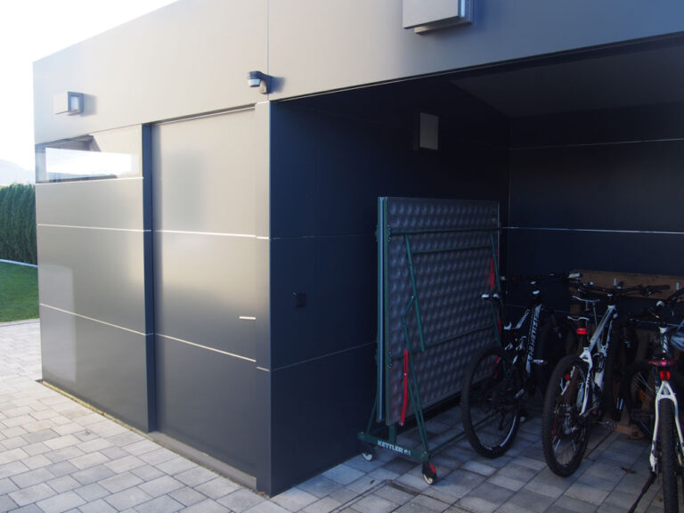 Zwei Fahrräder stehen unter einem modernen Carport neben einem Gitter, gepflasterter Boden. HANSEL.kraus metalltechnik gmbh