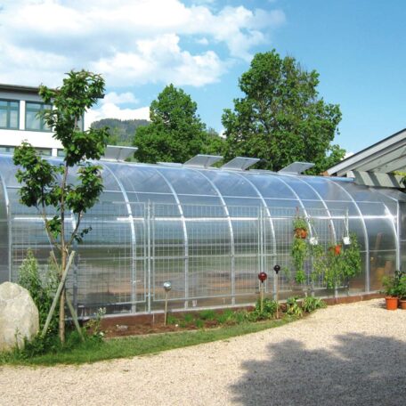 Ein modernes Gewächshaus aus Glas mit Pflanzen neben einem Gebäude bei Sonnenschein. HANSEL.kraus metalltechnik gmbh