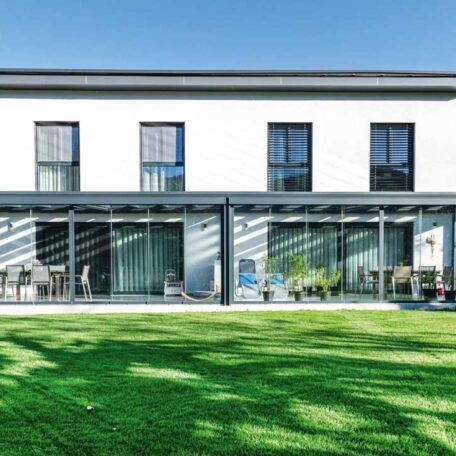 Modernes zweistöckiges Haus mit großen Fenstern und gepflegtem Garten bei strahlendem Sonnenschein. HANSEL.kraus metalltechnik gmbh