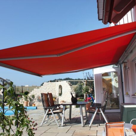 Große rote Markise spendet Schatten über Terrasse mit Gartenmöbeln an sonnigem Tag. HANSEL.kraus metalltechnik gmbh