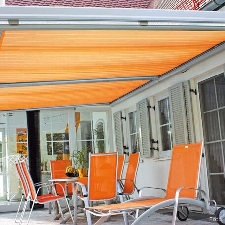 Terrasse mit orangefarbener Markise und passenden Stühlen an Fensterfront eines Hauses. de HANSEL.kraus metalltechnik gmbh