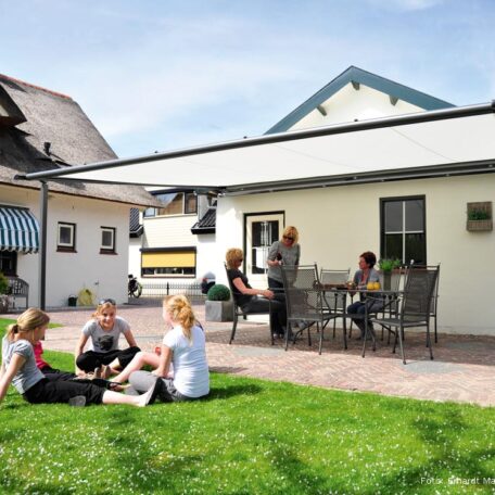 Familie sitzt entspannt im Garten unter Markise, Austausch und Freizeit an sonnigem Tag. de HANSEL.kraus metalltechnik gmbh