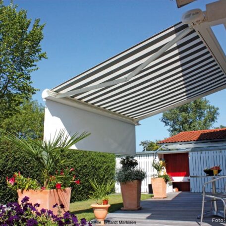 Markise spendet Schatten auf Terrasse mit Blumentöpfen und Garten, Sommerstimmung. HANSEL.kraus metalltechnik gmbh
