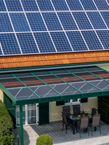 Solaranlage auf Hausdach mit überdachter Terrasse und Gartenmöbeln, sonniges Wetter. HANSEL.kraus metalltechnik gmbh