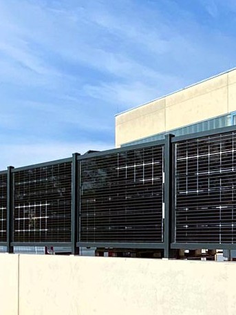 Mehrere Solarpanels als Zaun vor modernem Gebäude an sonnigem Tag installiert. HANSEL.kraus metalltechnik gmbh
