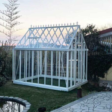 Weißes Gewächshaus aus Glas steht im Garten neben einem kleinen Teich bei Sonnenuntergang. HANSEL.kraus metalltechnik gmbh