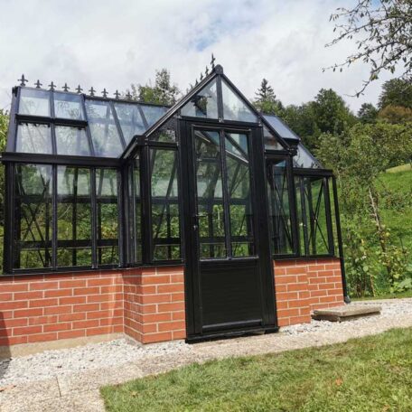 Glashaus mit schwarzem Rahmen auf gemauertem Sockel steht im grünen Garten. HANSEL.kraus metalltechnik gmbh