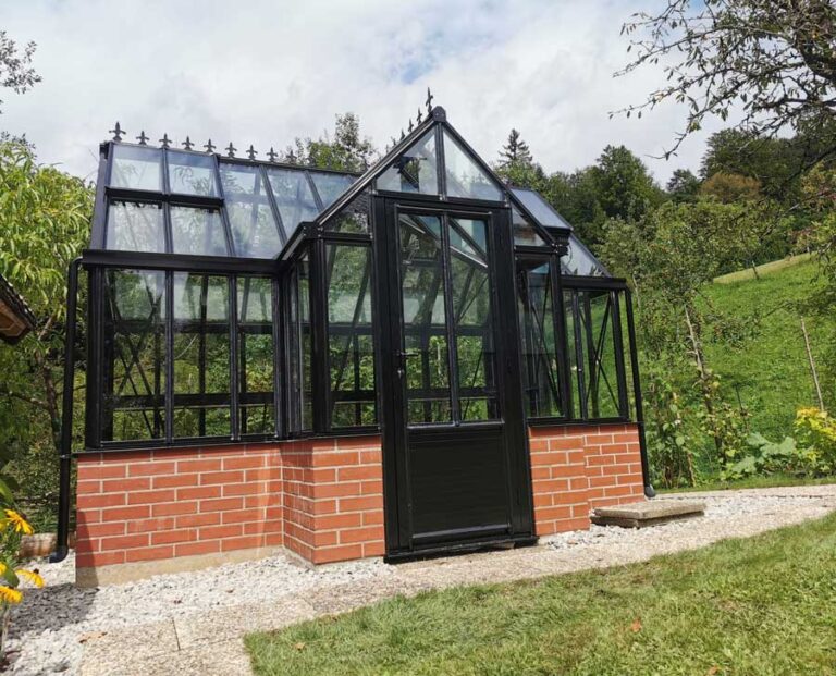 Glashaus mit schwarzem Rahmen auf gemauertem Sockel steht im grünen Garten. HANSEL.kraus metalltechnik gmbh