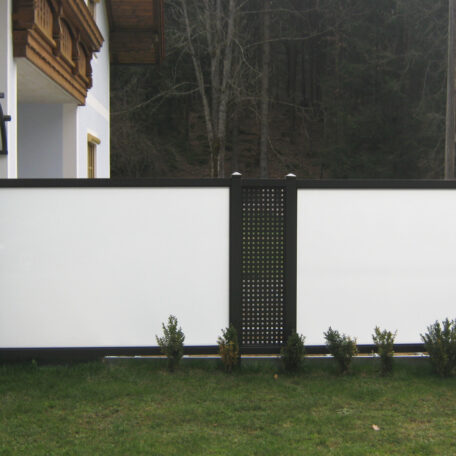 Weiße Sichtschutzwand mit schwarzem Tor, davor grüne Büsche und Rasenfläche. de HANSEL.kraus metalltechnik gmbh