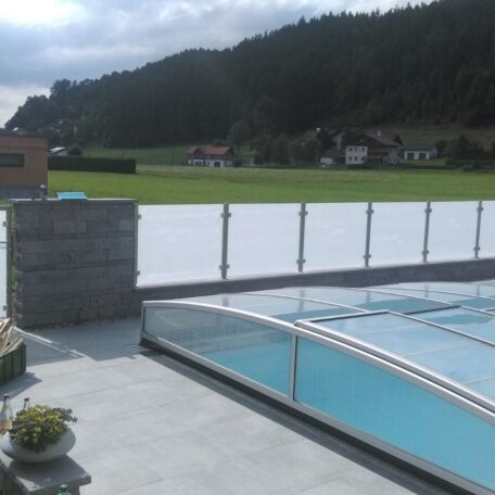 Geschützter Pool mit Glasüberdachung auf Terrasse, im Hintergrund grüne Wiesen und Berge. HANSEL.kraus metalltechnik gmbh