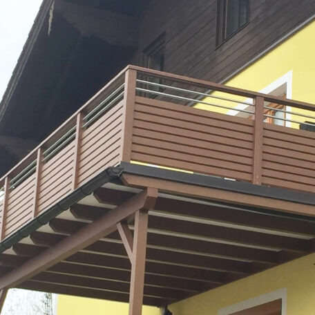 Balkon mit braunem Holzgeländer an gelber Hausfassade, darunter Stützpfeiler. de HANSEL.kraus metalltechnik gmbh