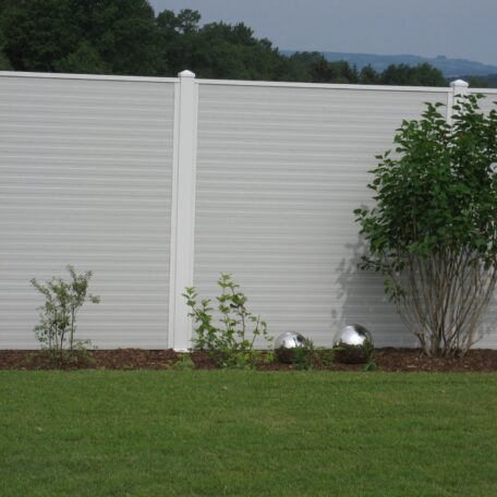Weiße Sichtschutzwand im Garten, davor grüne Rasenfläche und einige Büsche. HANSEL.kraus metalltechnik gmbh