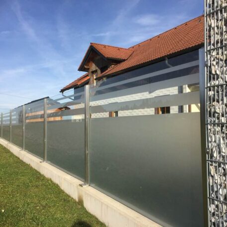 Moderner Sichtschutzzaun aus Glas und Metall vor einem Wohnhaus mit Gabionenelement. HANSEL.kraus metalltechnik gmbh
