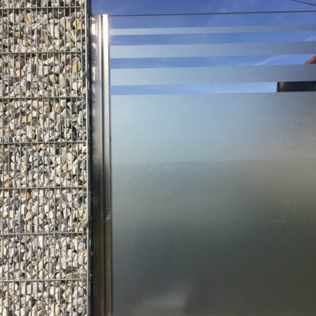 Strukturierte Betonwand neben halbtransparenter Glasfläche mit silbernem Rahmen im Außenbereich. HANSEL.kraus metalltechnik gmbh