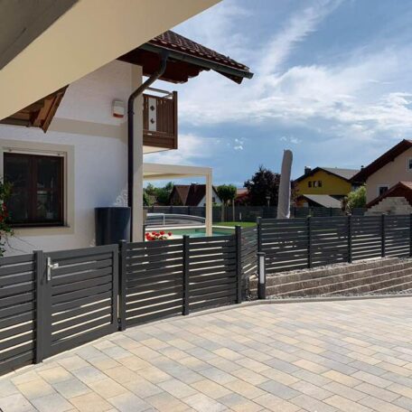 Modernes Wohnhaus mit dunkelgrauem Gartenzaun und gepflasterter Einfahrt an sonnigem Tag. de HANSEL.kraus metalltechnik gmbh