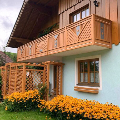 Holzbalkon und Rankgitter an Hausfassade mit blühenden gelben Blumen im Vorgarten. HANSEL.kraus metalltechnik gmbh