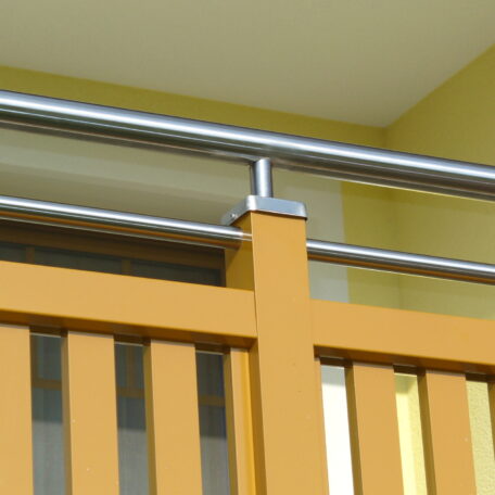 Modernes Balkongeländer aus Edelstahl und Holz vor gelber Wand, Detailansicht. HANSEL.kraus metalltechnik gmbh