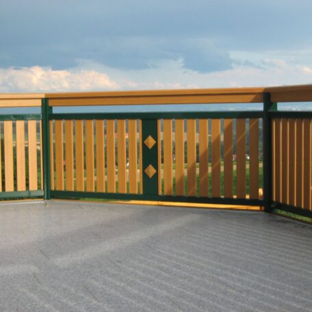 Holzgeländer mit grünen Elementen auf Terrasse, Blick in Landschaft unter bewölktem Himmel. HANSEL.kraus metalltechnik gmbh