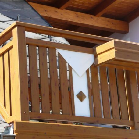 Holzbalkon mit dekorativem weißem Element an Hausfassade unter einem Dach. HANSEL.kraus metalltechnik gmbh