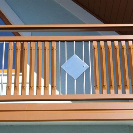 Holzgeländer mit vertikalen Streben und mittigem, quadratischem Metallelement auf Balkon. HANSEL.kraus metalltechnik gmbh