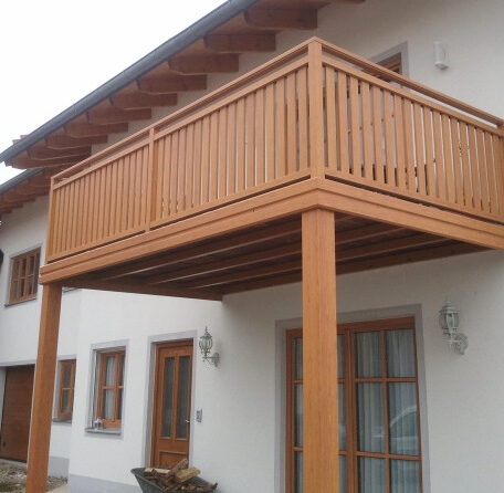 Holzbalkon mit senkrechten Streben an weißem Einfamilienhaus, Eingangsbereich darunter. HANSEL.kraus metalltechnik gmbh